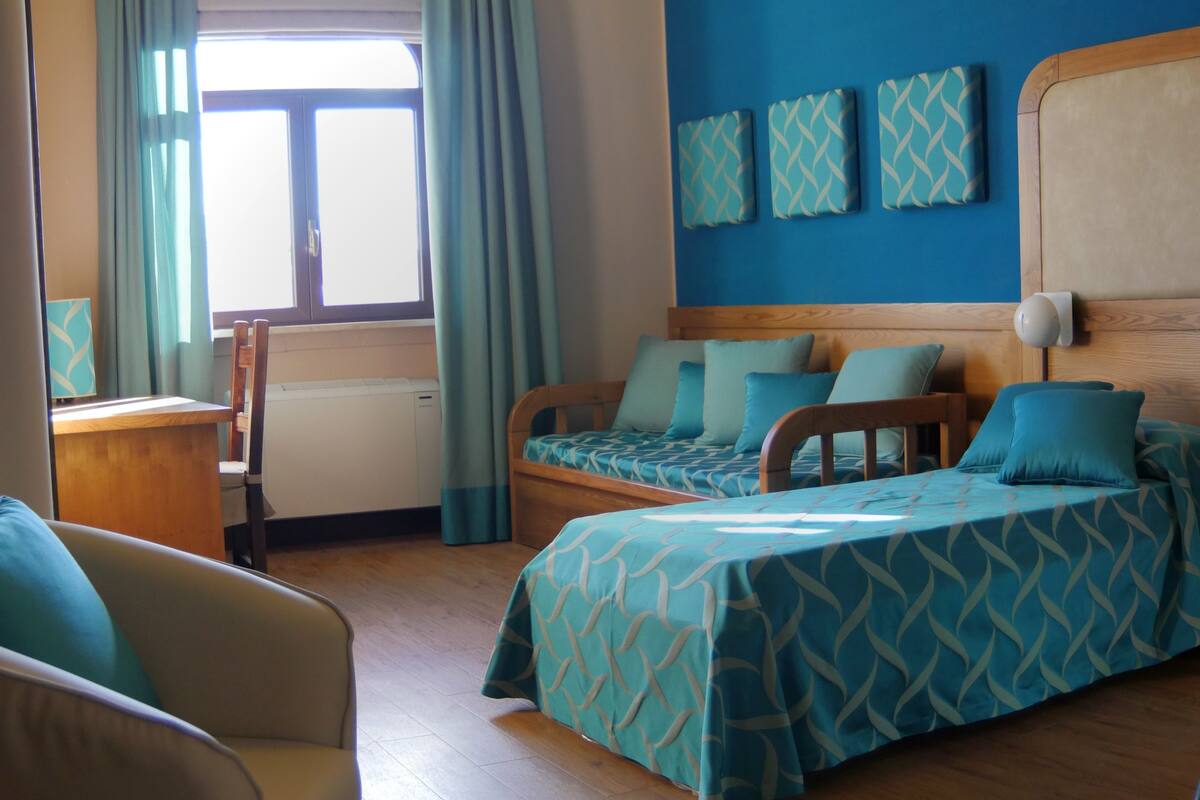 Ein Hotelzimmer mit zwei Betten, einem Schreibtisch, einem Stuhl und einem Fenster mit Vorhängen.