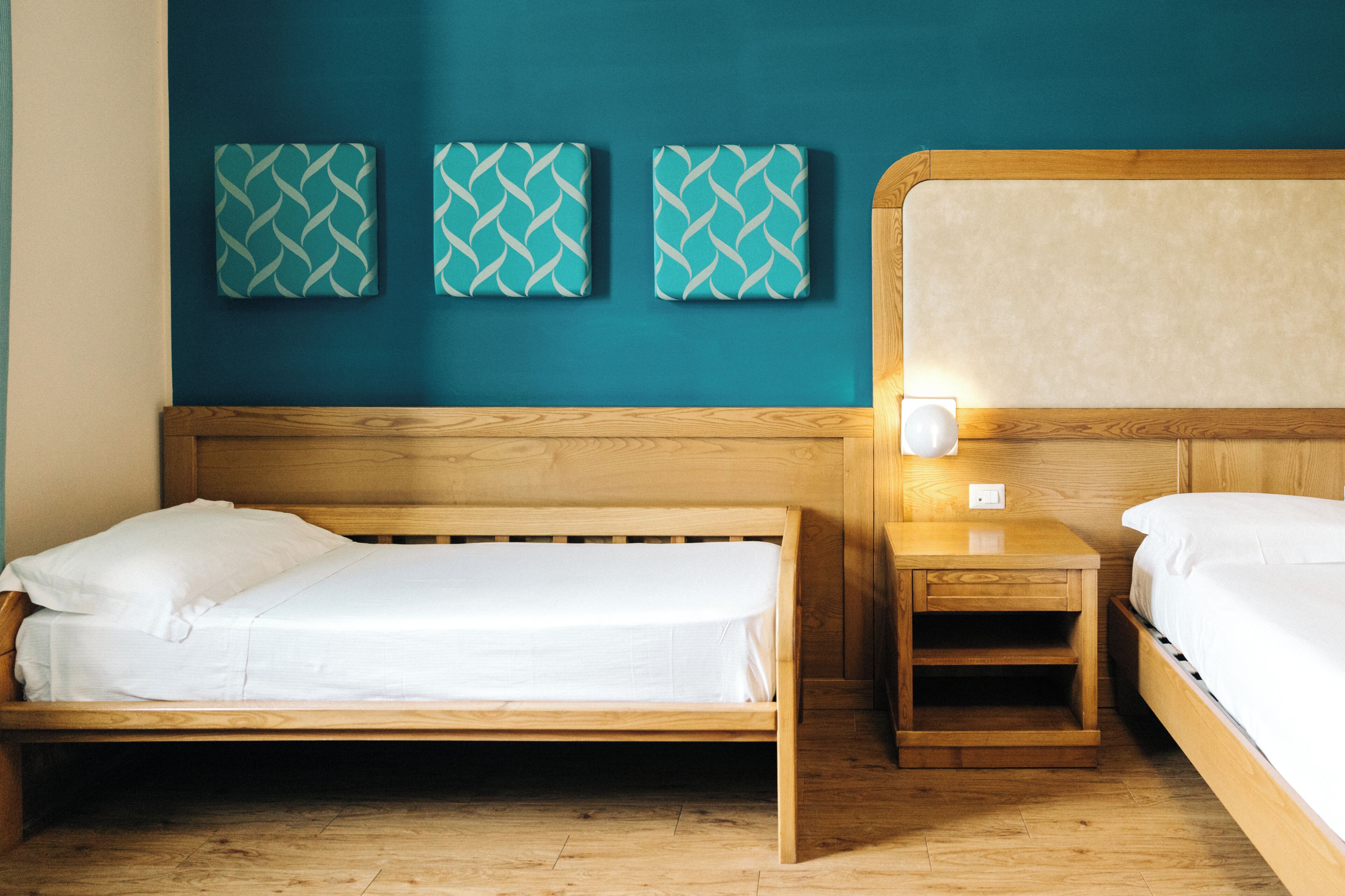 Una habitación con dos camas de madera, una mesita de noche con lámpara y tres obras de arte decorativas en la pared.
