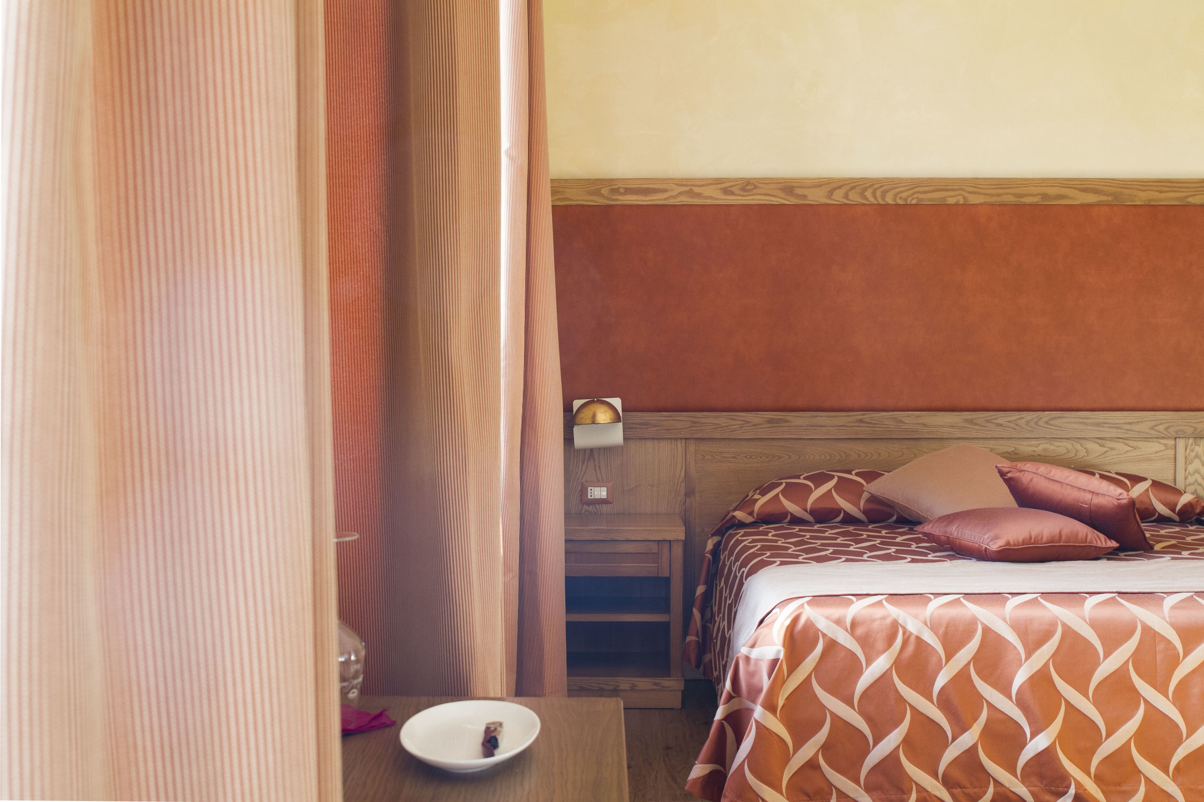 A hotel room with two beds, a bedside table with a lamp, and a curtain.