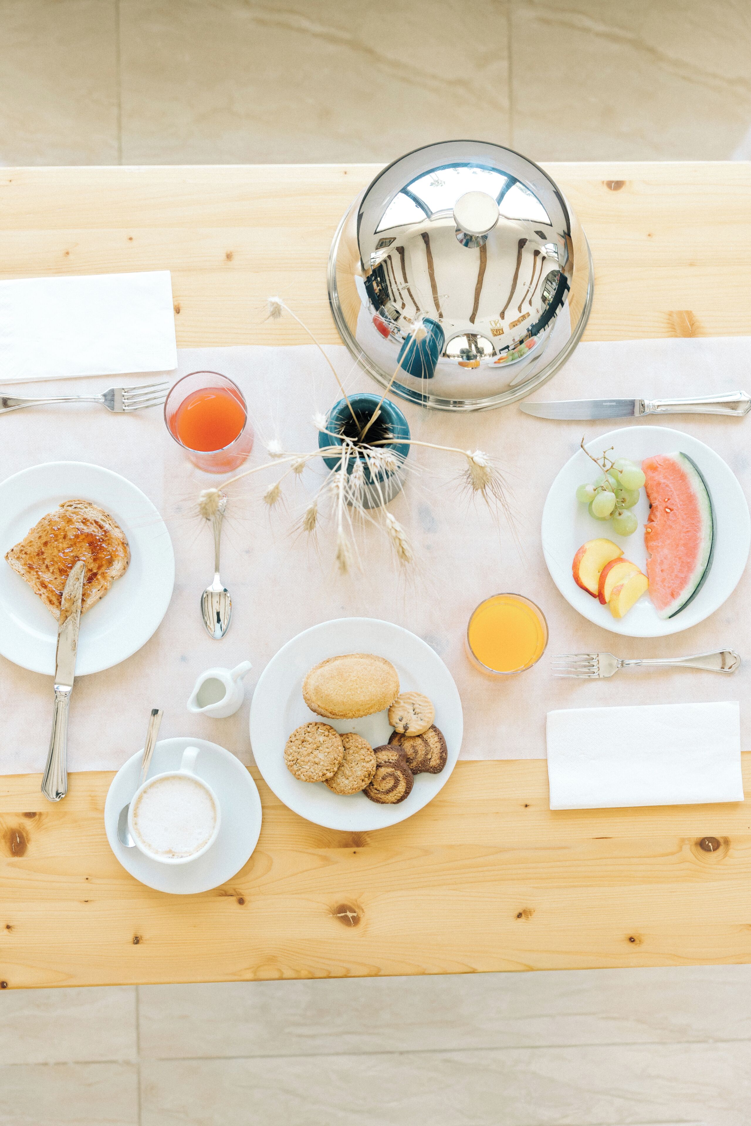 A breakfast table with a variety of food items, including toast, fruit, and cookies, along with a teapot and cups.