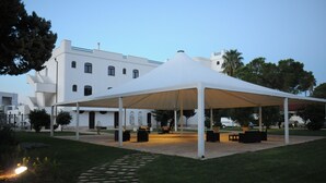 A white tented structure in a courtyard with a paved walkway, surrounded by greenery and a building in the background. - Leone De Castris Wine Hotel (Salice Salentino)