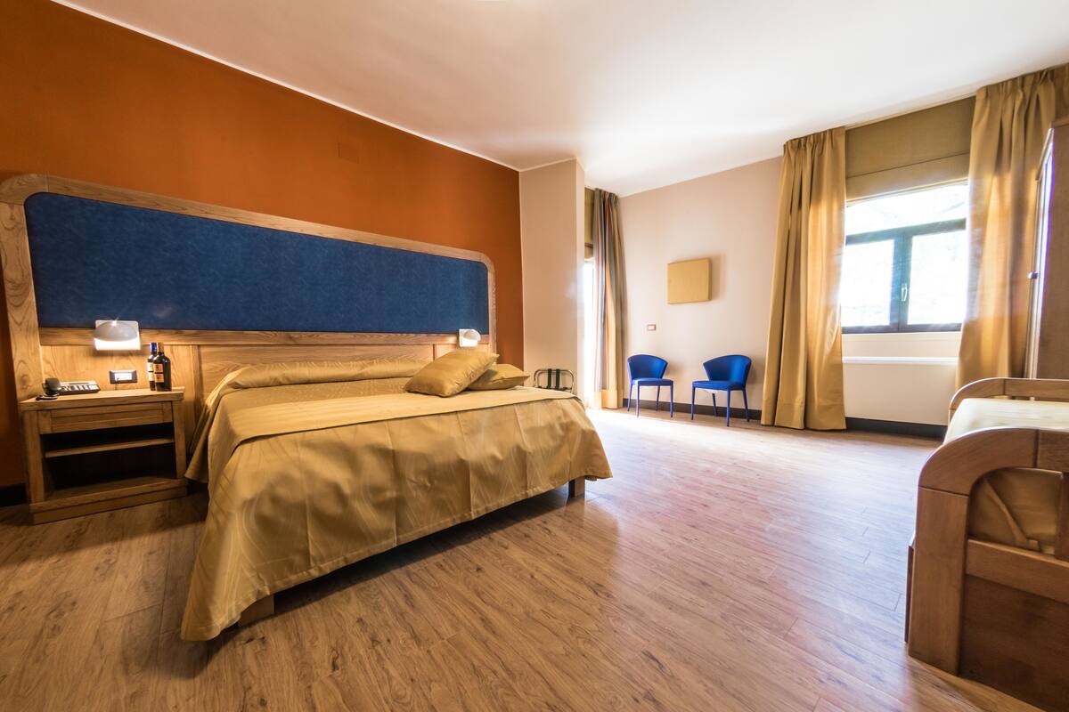 Ein Hotelzimmer mit einem großen Bett, einem Holznachttisch, einem Sessel und einem Schreibtisch.