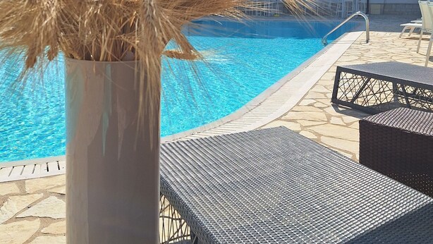 A poolside setting with a vase of dried plants, a red candle, and outdoor furniture. - Leone De Castris Wine Hotel (Salice Salentino)