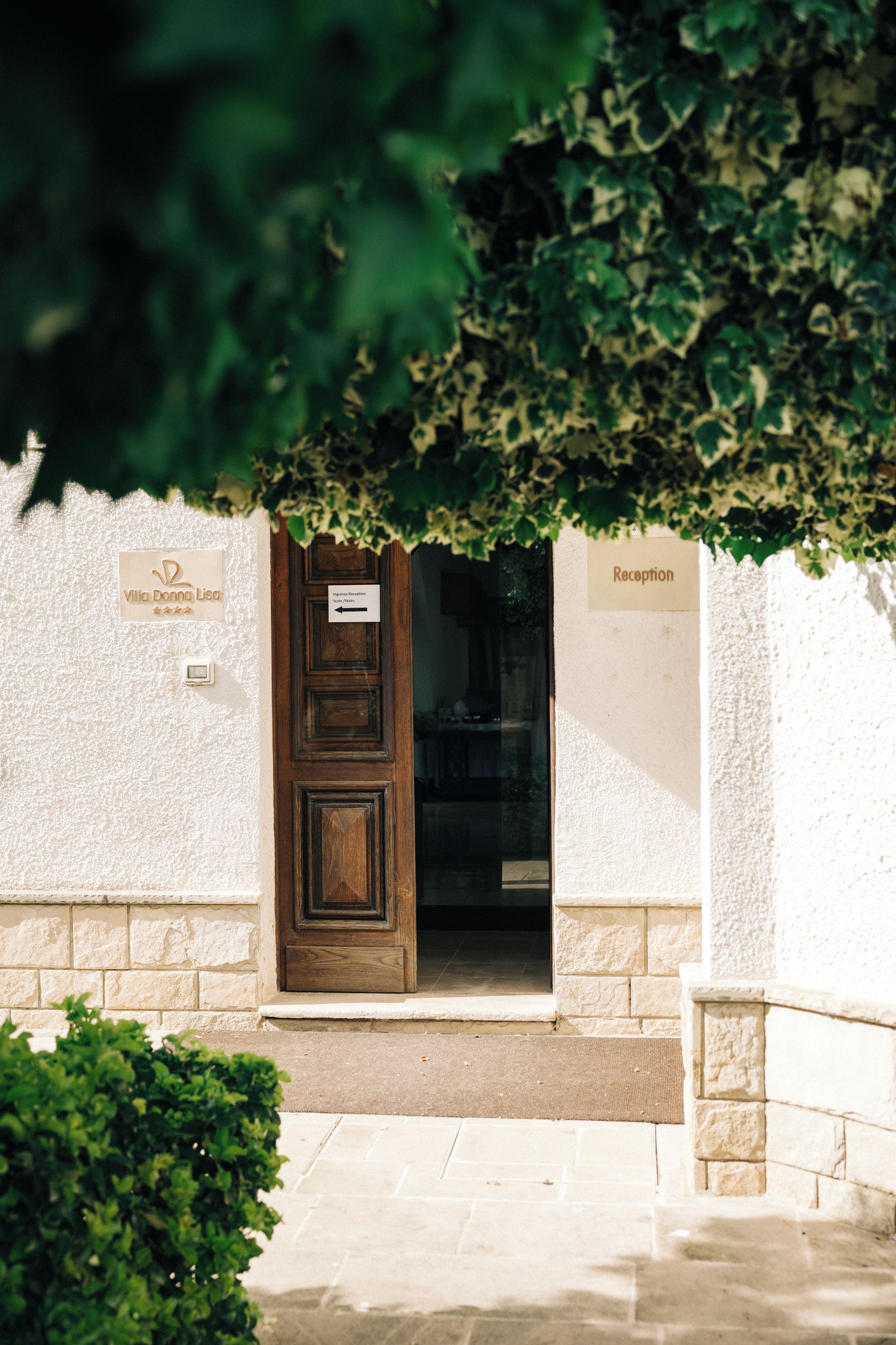 Un área de recepción con una puerta de madera, un cartel que dice 'Villa Donna Lisa' y un cartel que indica 'Recepción'.