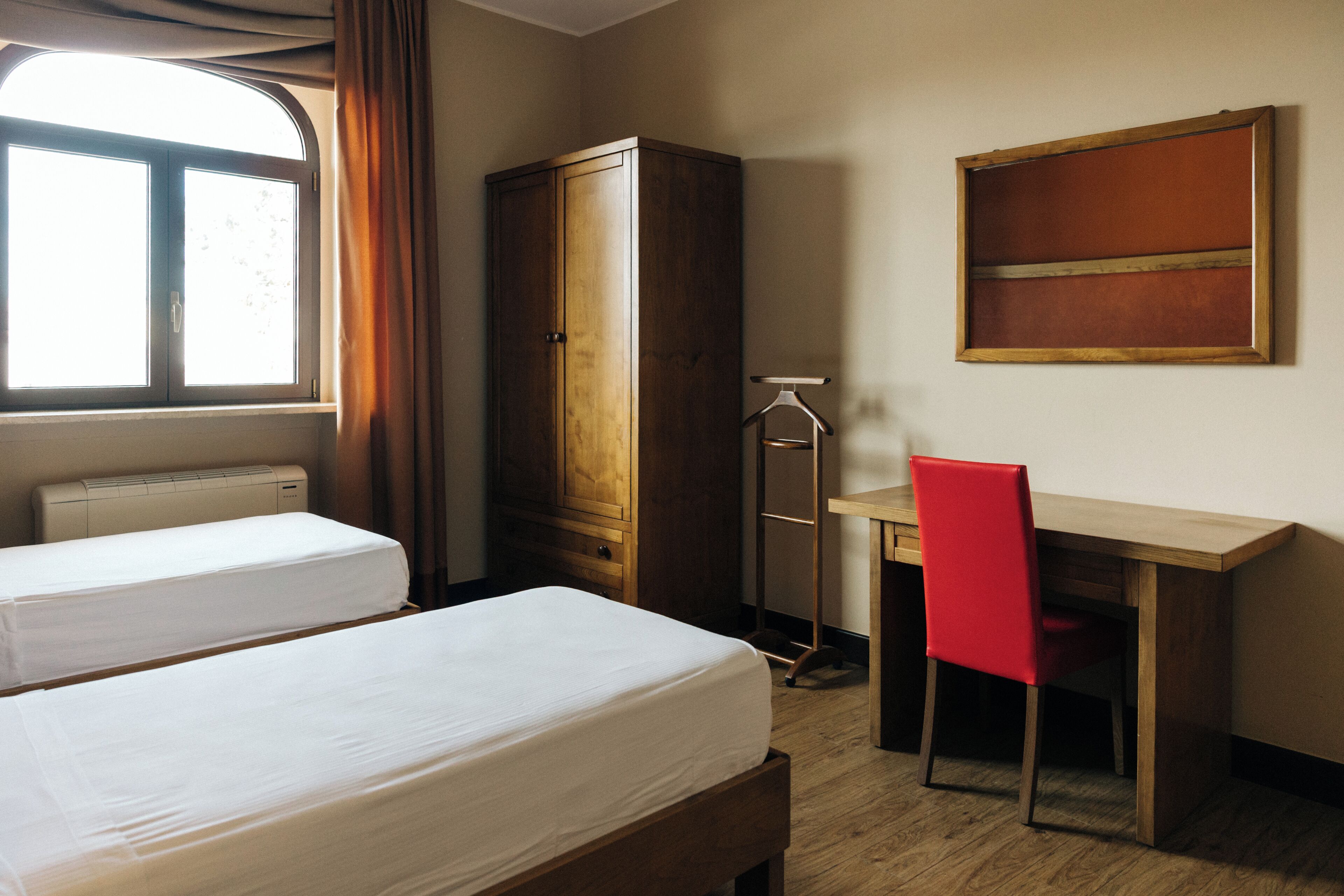 Une chambre d’hôtel avec deux lits, un bureau, une chaise, une armoire et un tableau au mur.