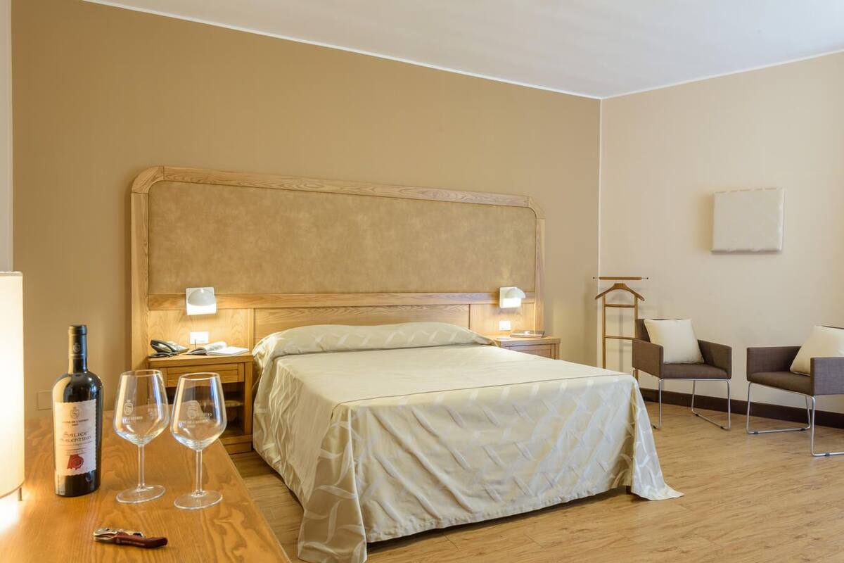 Ein Hotelzimmer mit Bett, Nachttischen, einem Sessel und einer Weinflasche.
