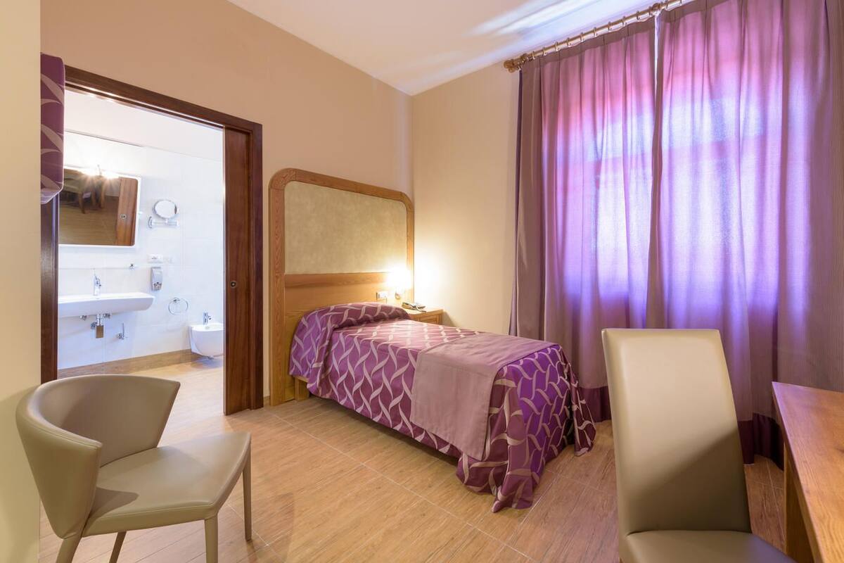 Ein Hotelzimmer mit einem Bett, zwei Sesseln, einem Schreibtisch, einem Spiegel und einem durchgegangenen Tür sichtbaren Badezimmer.