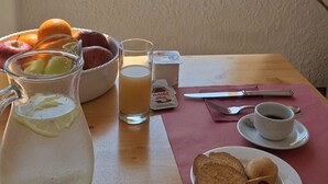 A breakfast table with a pitcher of lemonade, a glass of orange juice, a bowl of fruit, a Nutella packet, a cup of coffee, and a plate with cookies. - Leone De Castris Wine Hotel (Salice Salentino)