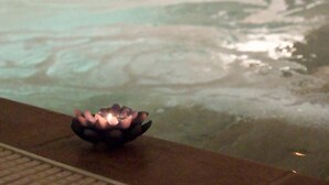 A person in a swimming pool with a lotus-shaped candle on the edge. - Carlo's Hotel (Castagneto Carducci)