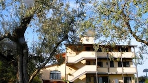 A multi-story building with a central staircase, surrounded by greenery and a large tree. - Carlo's Hotel (Castagneto Carducci)