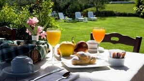 A breakfast setup with a croissant, apple, orange juice, and a basket of pastries on a table outdoors. - Carlo's Hotel (Castagneto Carducci)