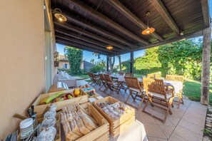 An outdoor dining area with wooden tables and chairs, a covered patio, and a variety of food items displayed on the tables. - Villa Carlotta Resort (Agrigento)