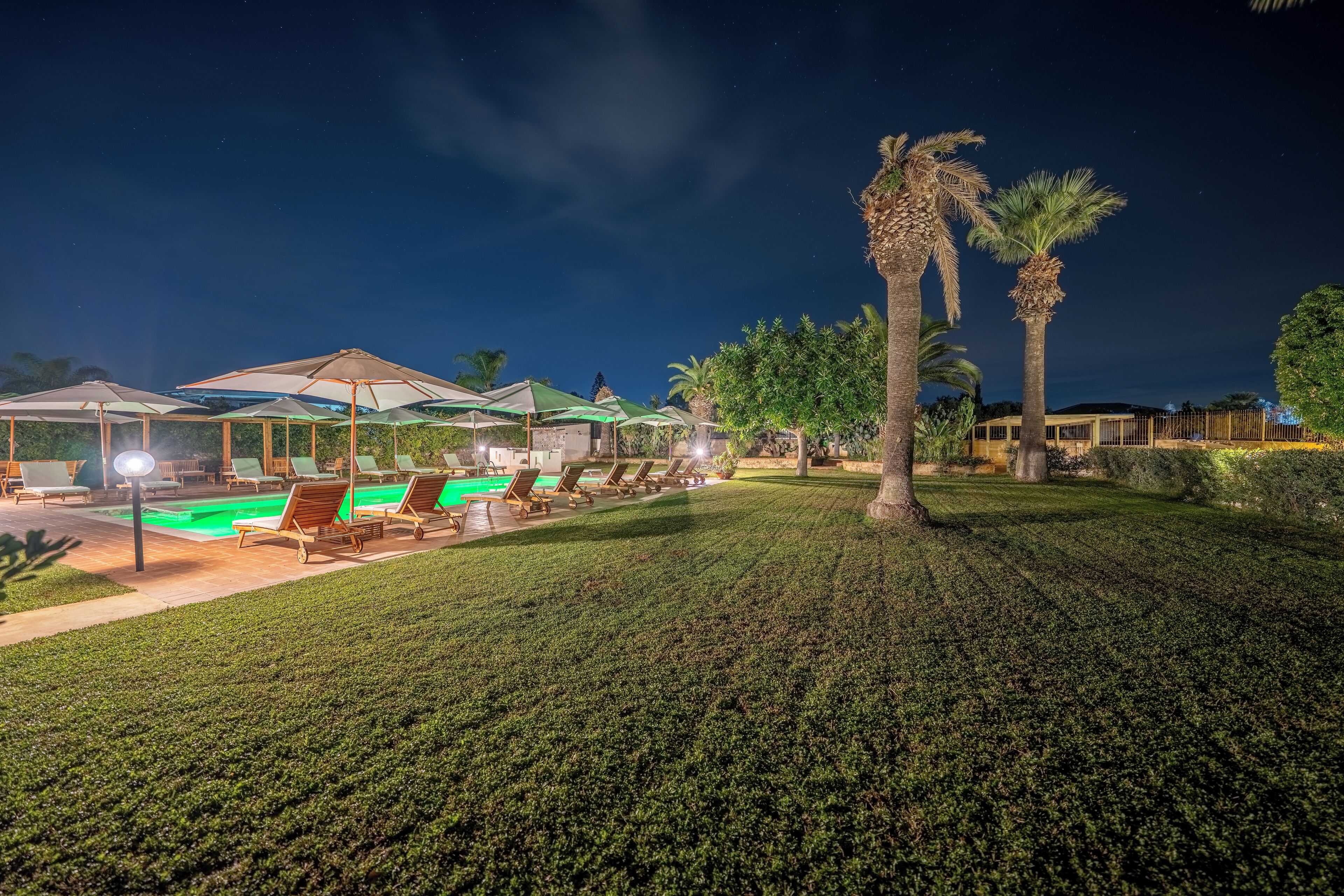 Un complex turístic de nit amb una piscina, gandules i palmeres.