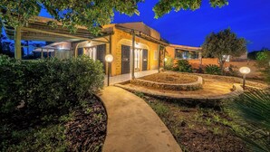 A well-lit house with a covered patio, surrounded by lush greenery and a stone pathway. - Villa Carlotta Resort (Agrigento)
