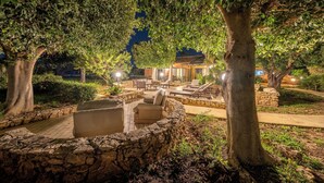 An outdoor seating area with stone walls and benches, surrounded by trees and a pathway leading to a building. - Villa Carlotta Resort (Agrigento)
