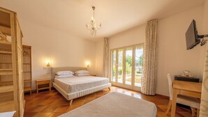 A bedroom with two beds, a chandelier, a TV, and a window with curtains. - Villa Carlotta Resort (Agrigento)