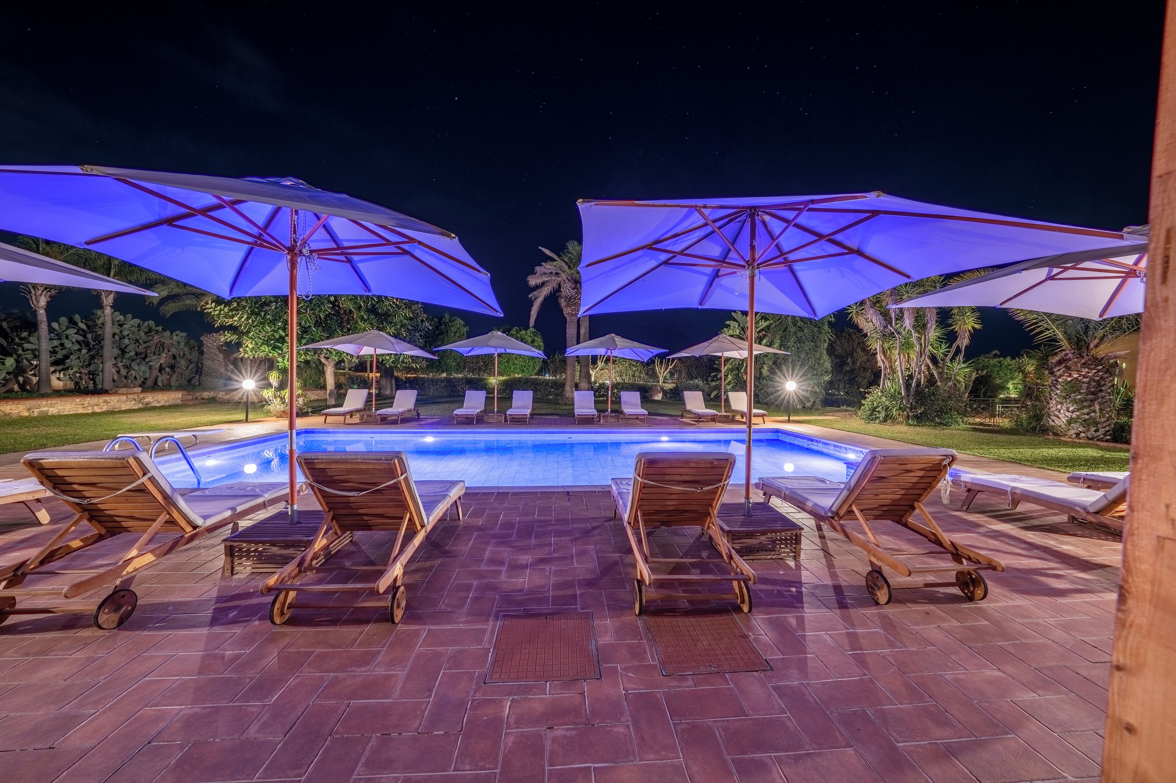 A poolside area with lounge chairs and umbrellas, a swimming pool, and a night sky.