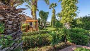 A well-maintained garden with palm trees, a wooden pergola, and a clear pathway. - Villa Carlotta Resort (Agrigento)
