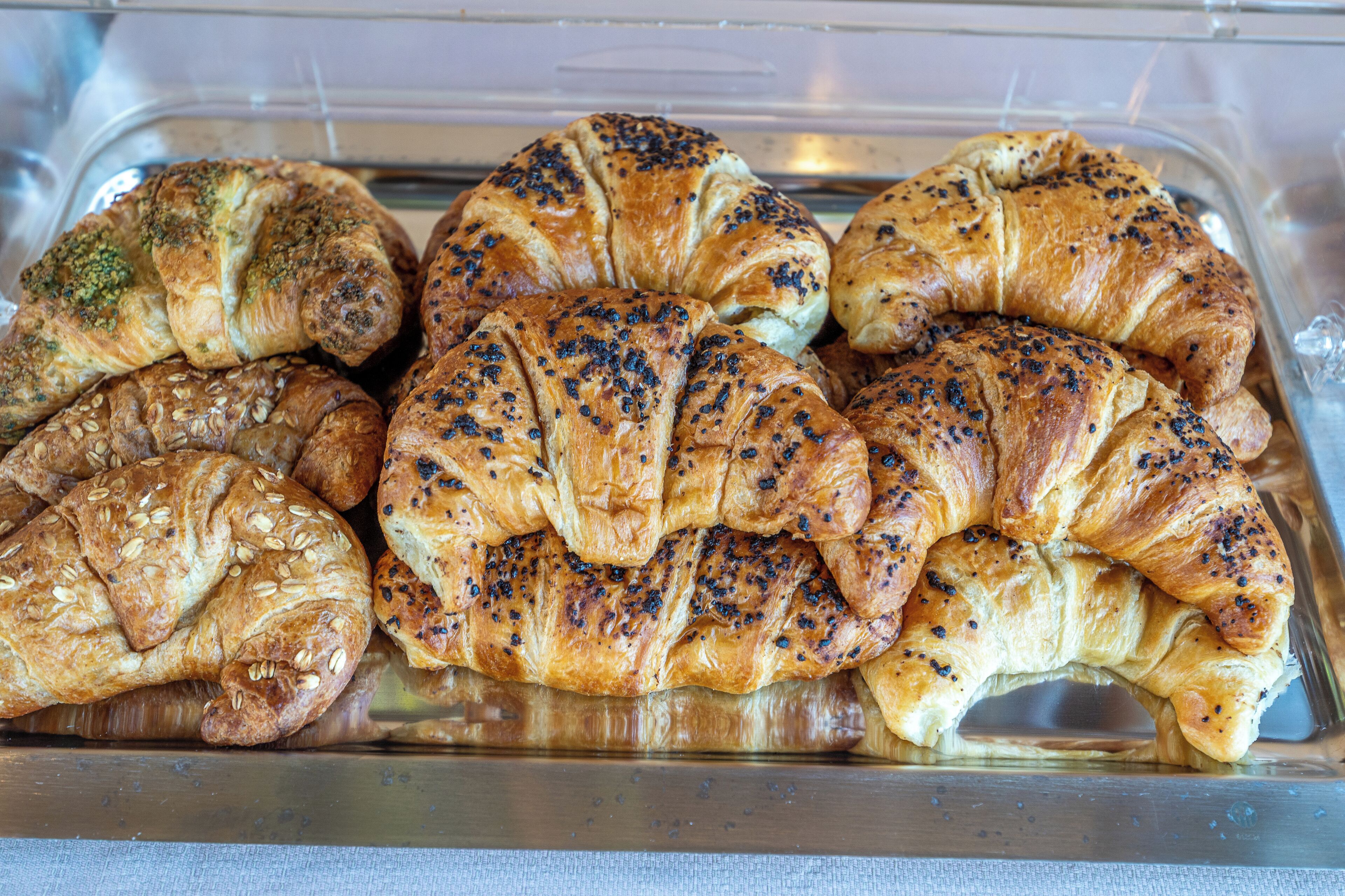 Eine Auswahl an Backwaren, darunter Croissants und Brötchen, präsentiert in einer transparenten Kunststoffschale.