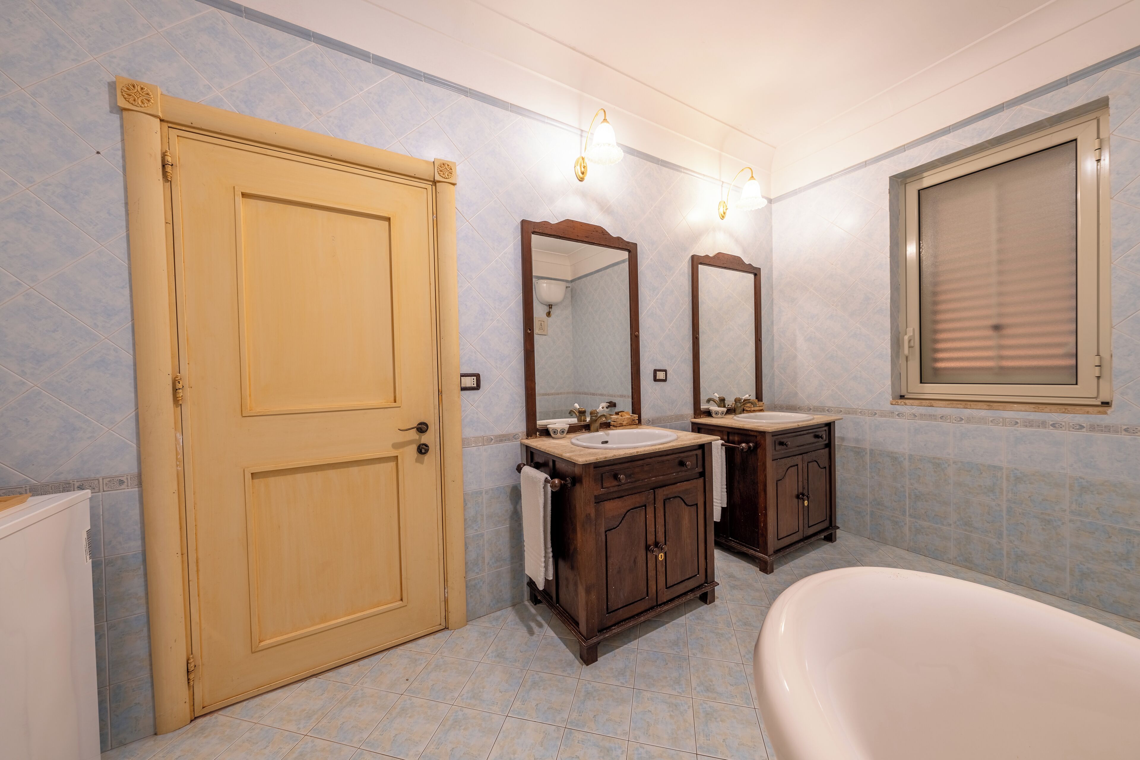 A bathroom with a wooden door, two sinks, a large mirror, and a bathtub.
