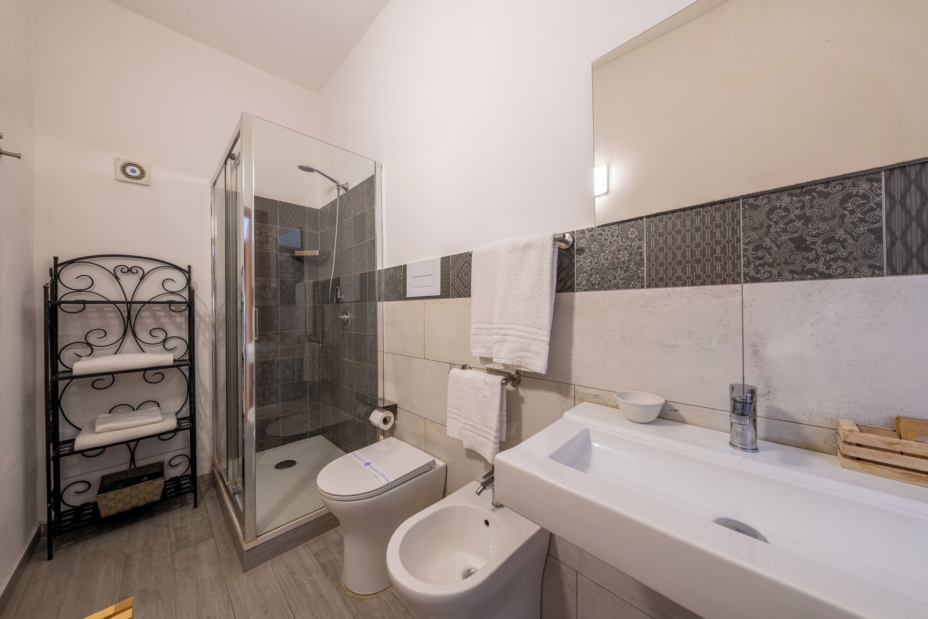 A modern bathroom with a glass shower enclosure, a toilet, bidet, and a white sink with a mirror.