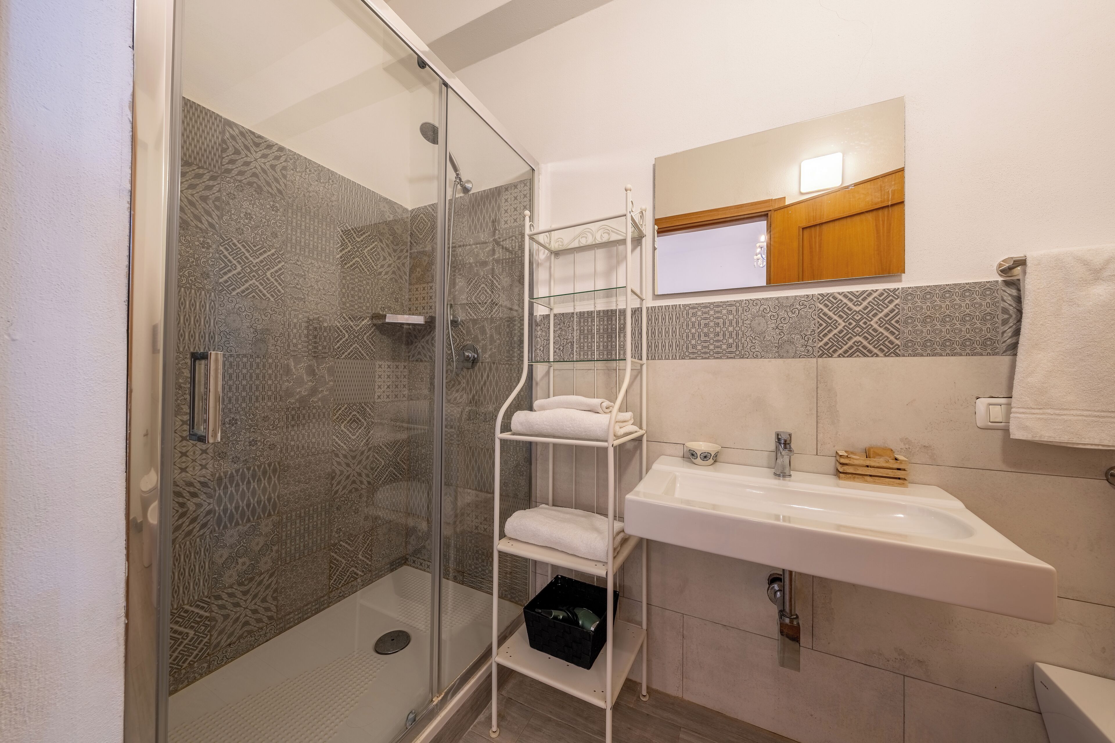 Un baño con cabina de ducha de vidrio, un lavabo blanco, un espejo y un perchero para toallas.