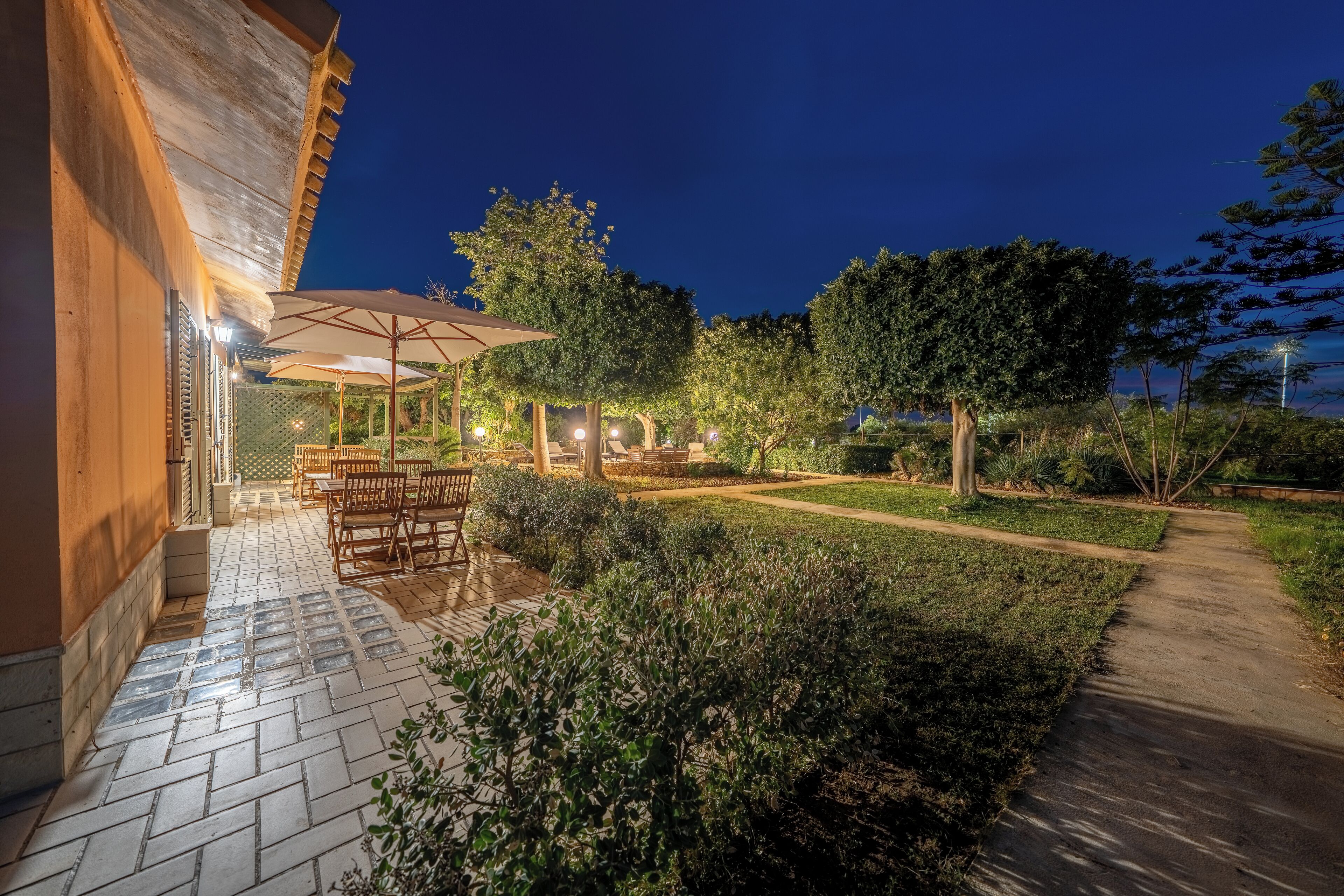 Eine Terrassenfläche mit Tisch und Stühlen, umgeben von Grünpflanzen und einem Weg.