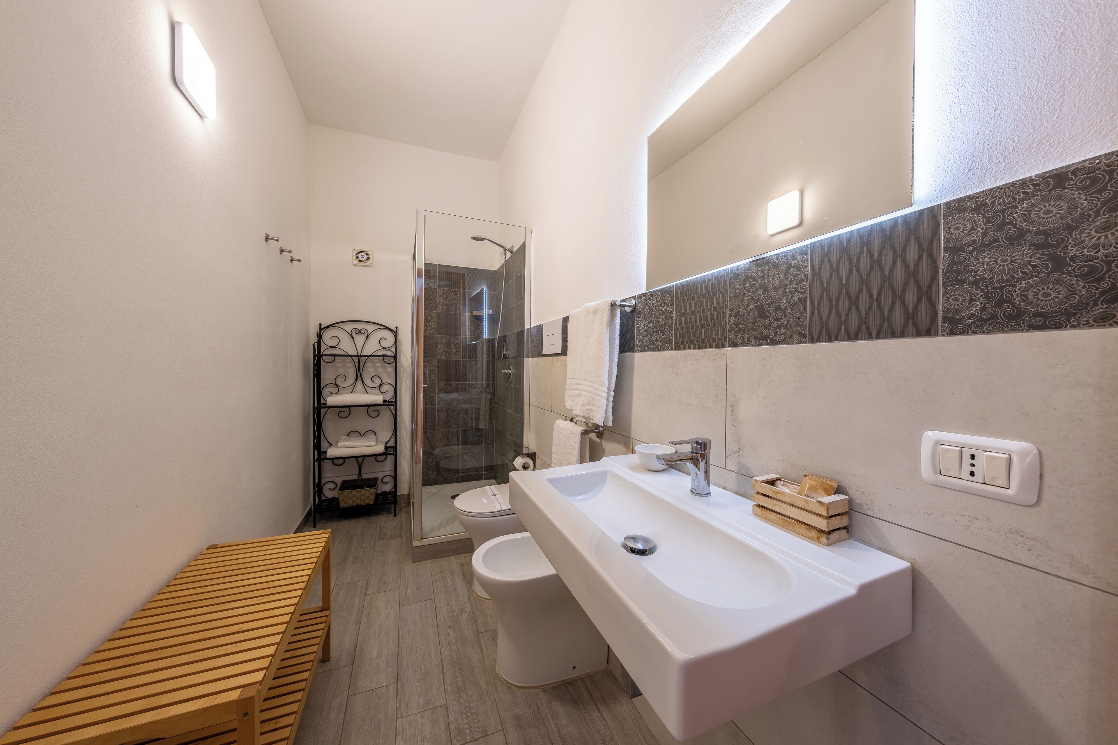 A modern bathroom with a wooden bench, a large sink, and a glass shower enclosure.