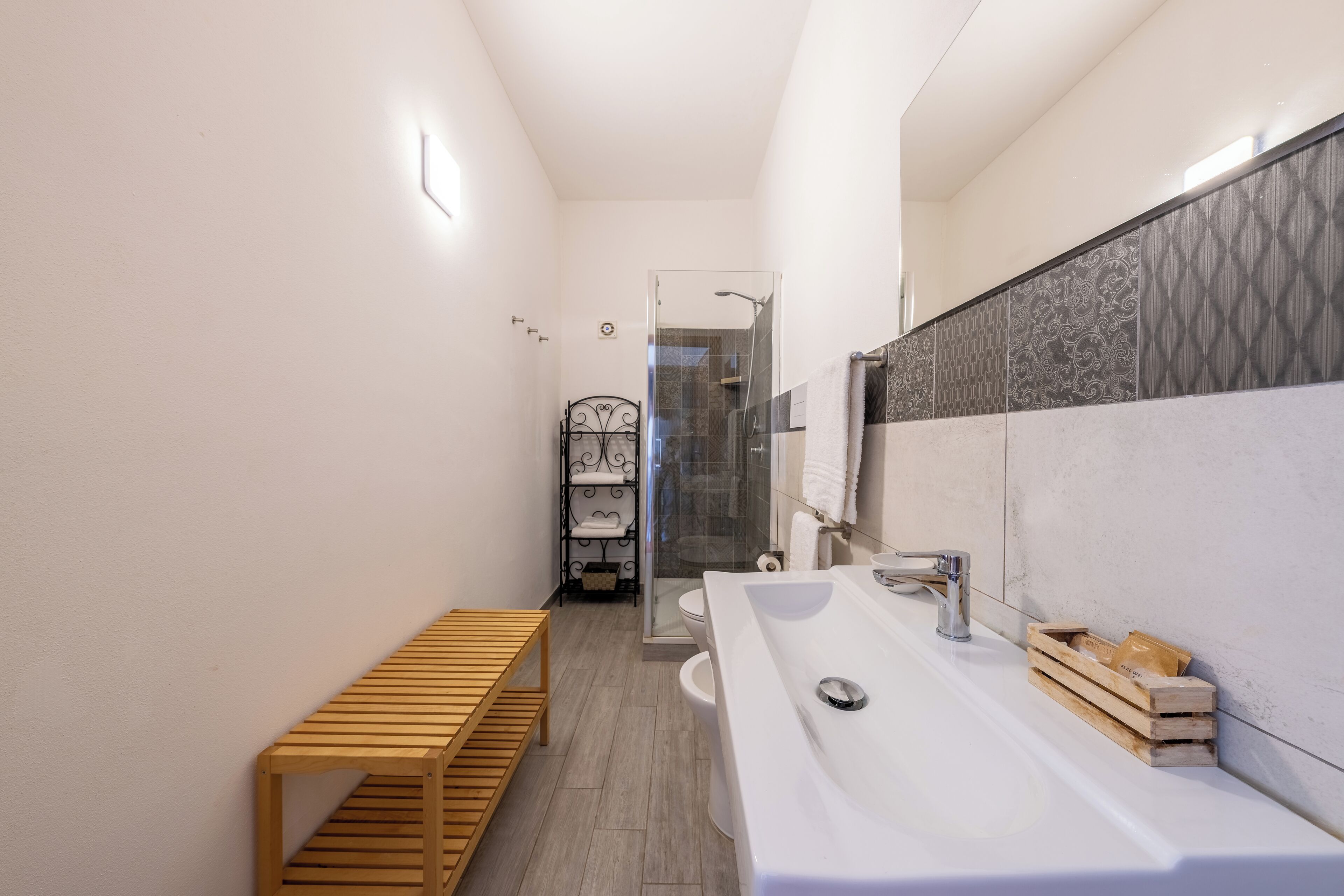 A modern bathroom with a large sink, a glass shower enclosure, and a wooden bench.