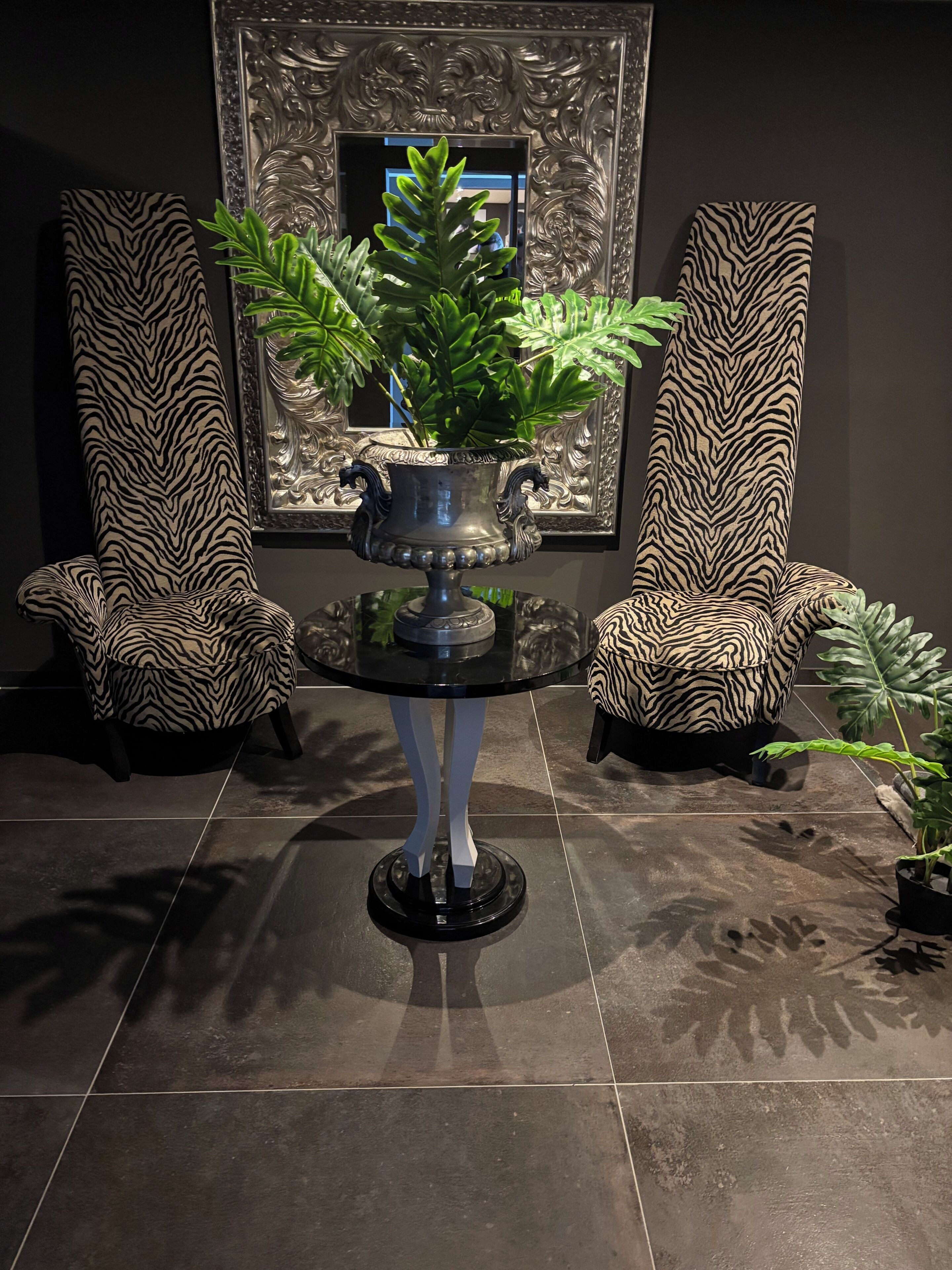 Una habitación con dos sillones de estampado de cebra, una mesa central con una planta en maceta y un espejo decorativo en la pared.