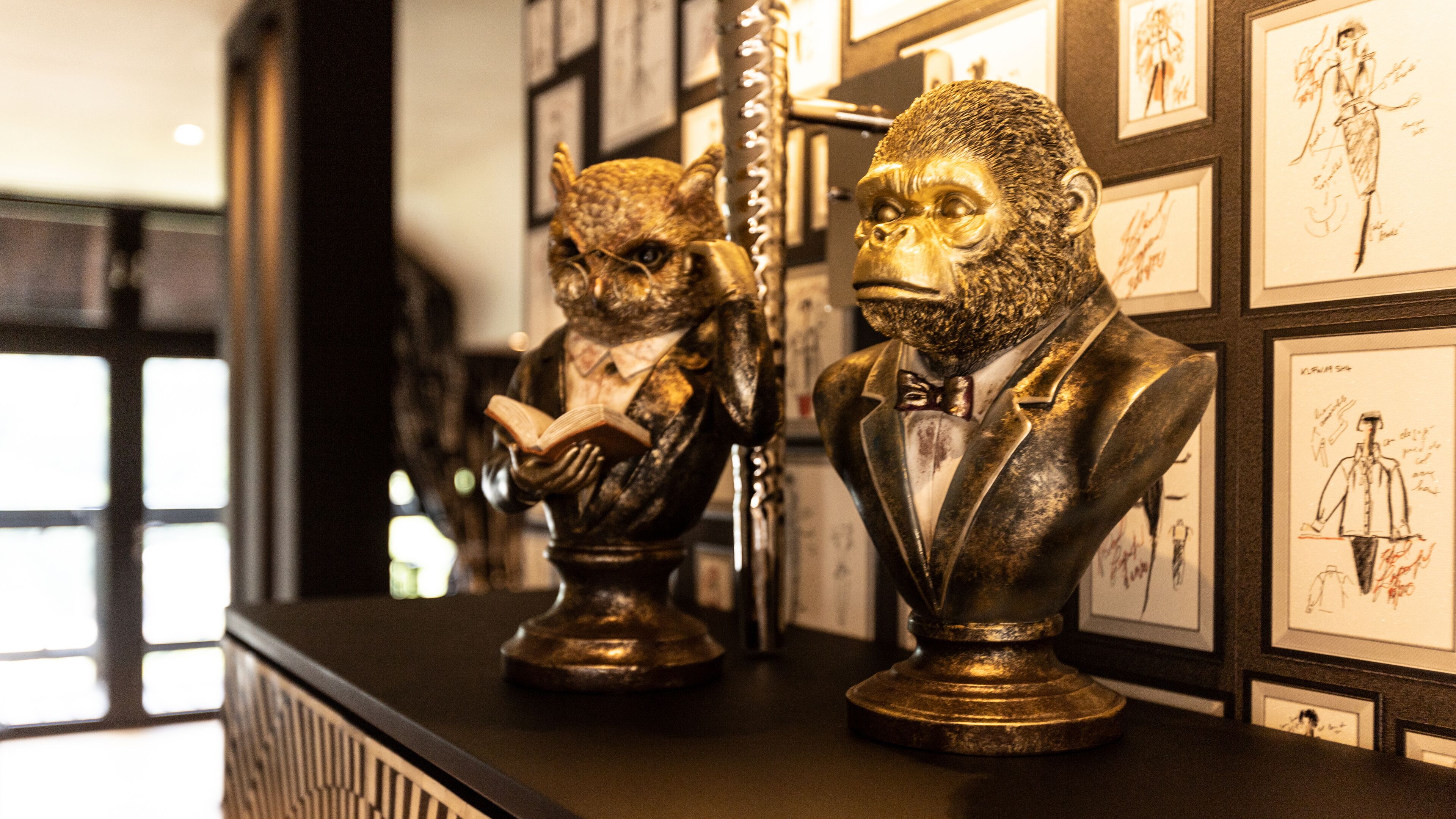 Two bronze busts on a black counter with framed sketches on the wall behind.