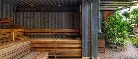 A wooden sauna with benches and a wooden floor, surrounded by a wooden deck and greenery.