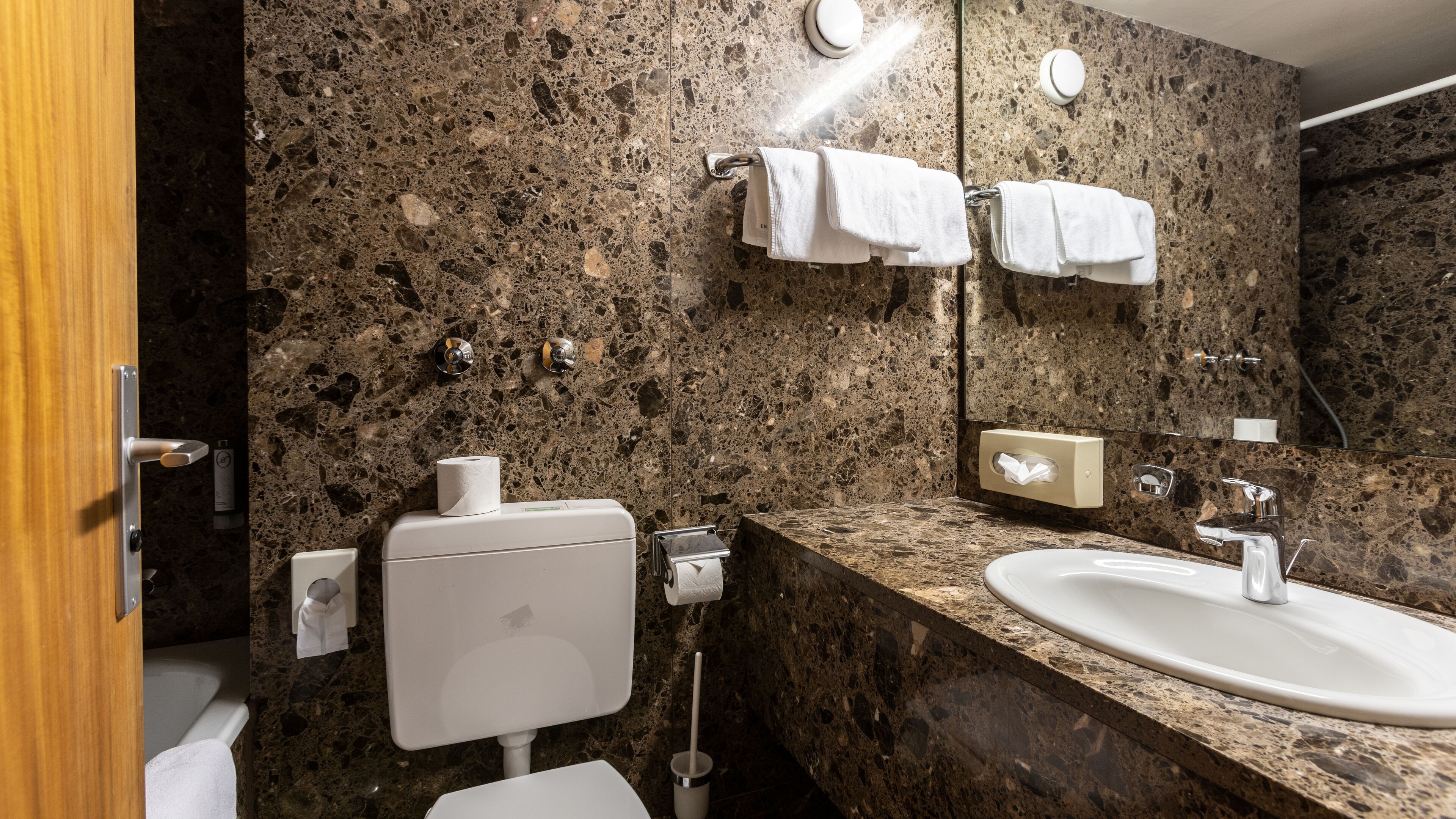 Ein Badezimmer mit Marmorwaschbecken, Toilette, Spiegel und Handtüchern, die an der Wand hängen.