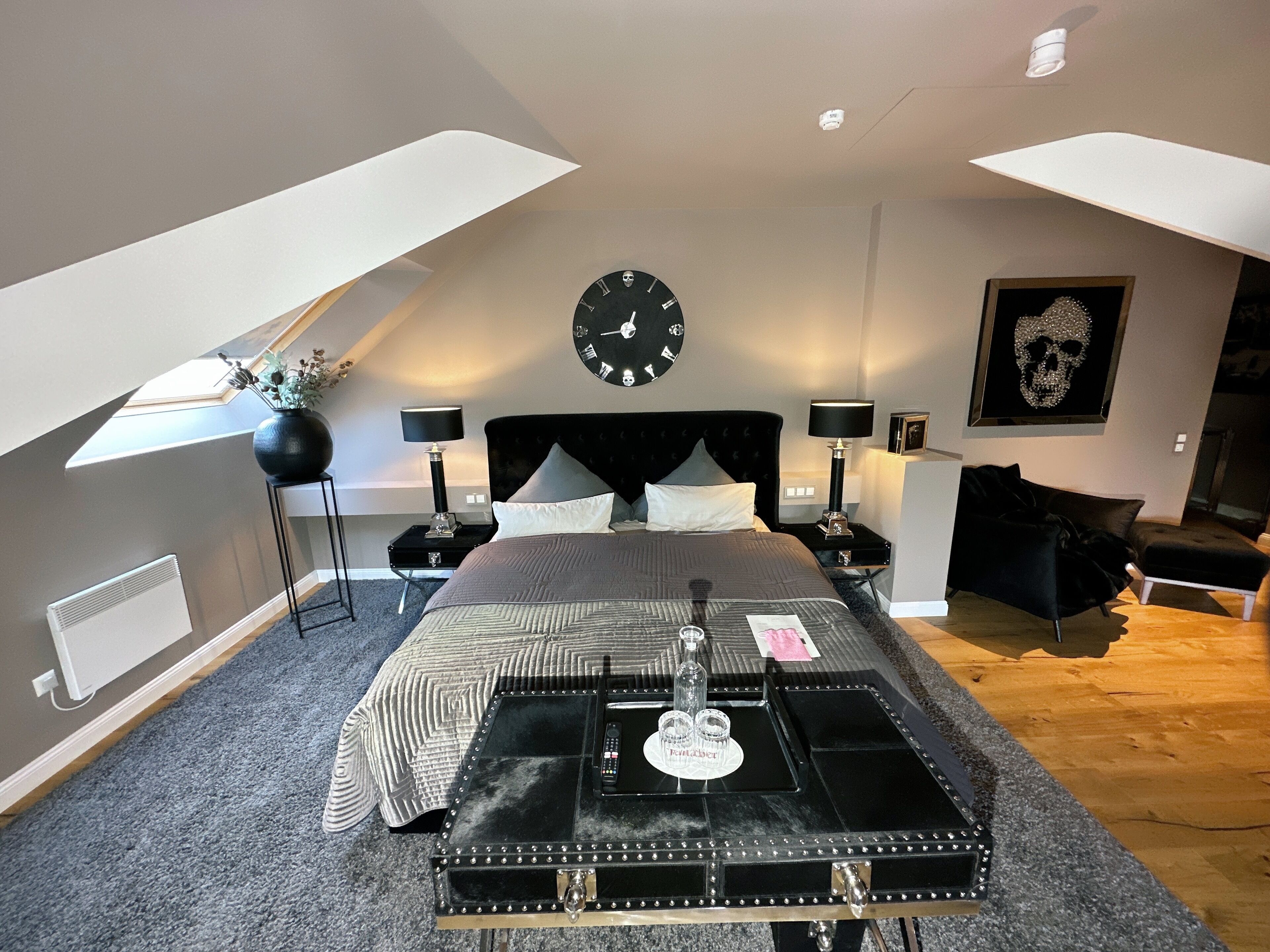 A modern bedroom with a large bed, a black clock on the wall, and a unique black table with a lock.
