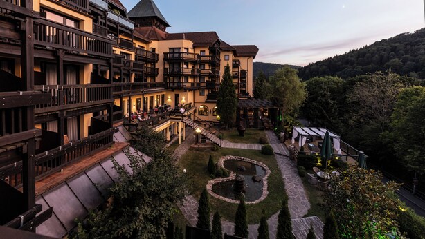 A multi-story hotel with balconies, a courtyard with a circular garden, and a mountain backdrop.
