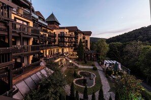 Een meerlaags hotel met balkons, een binnentuin met een ronde tuin en een berg op de achtergrond.