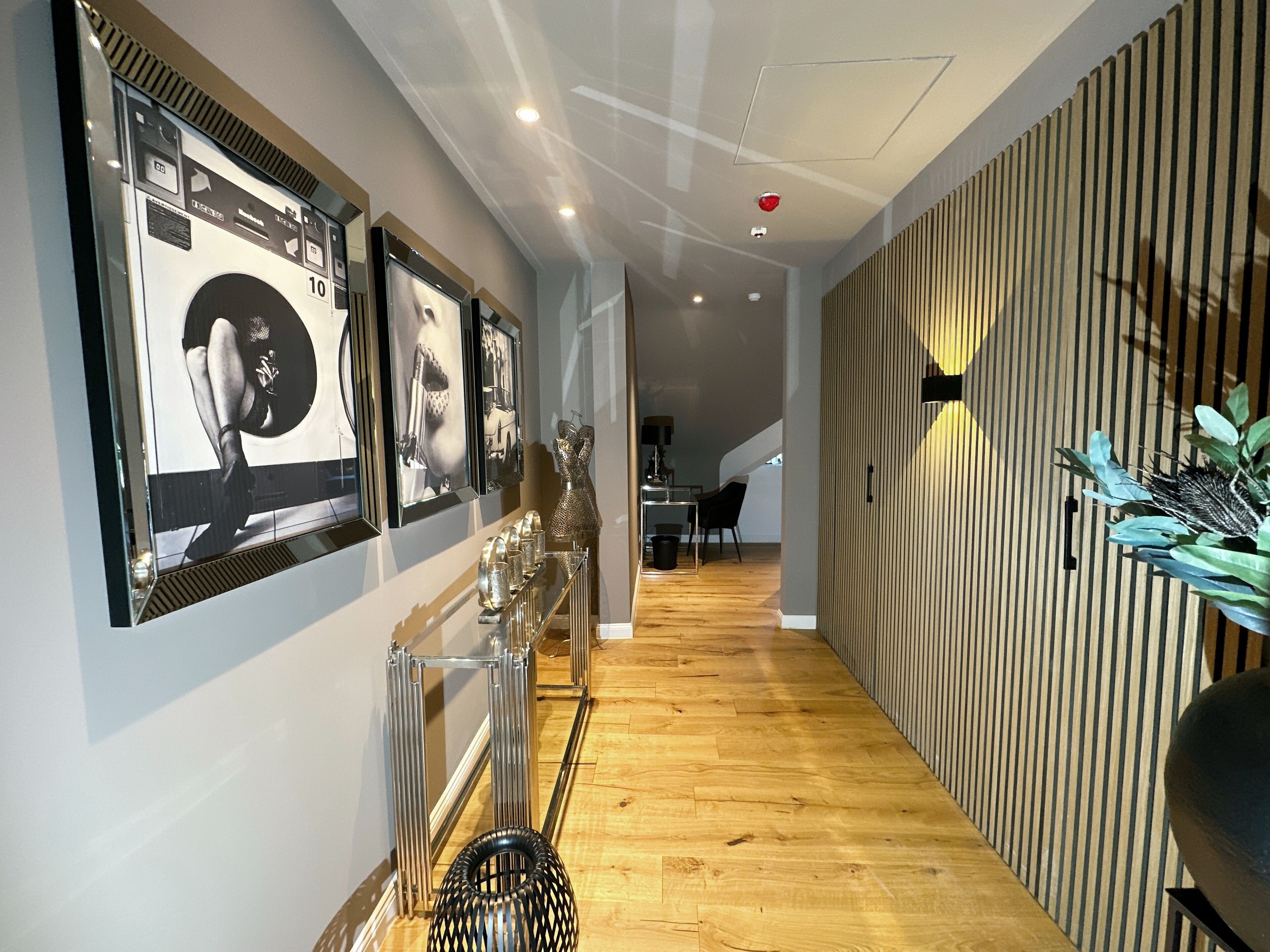 A hallway with wooden flooring, a metal rack with decorative items, and a wall with vertical wooden slats.