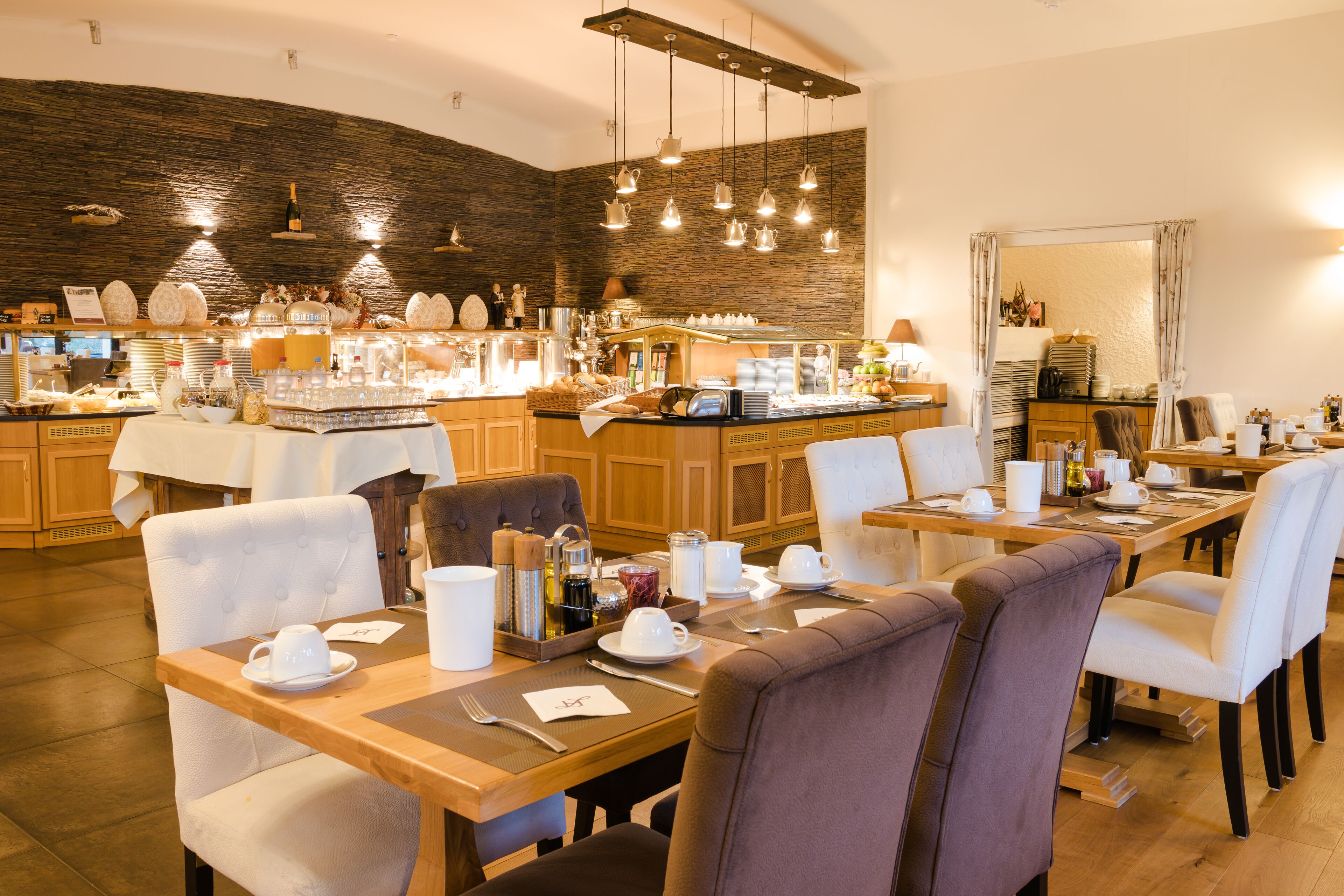 Un restaurante con mesas y sillas de madera, una zona de bar con diferentes opciones de comida y bebida, y una pared de piedra al fondo.