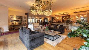 A spacious living area with a large sofa, a coffee table, and a fireplace. There is a stone fireplace surround and a chandelier.