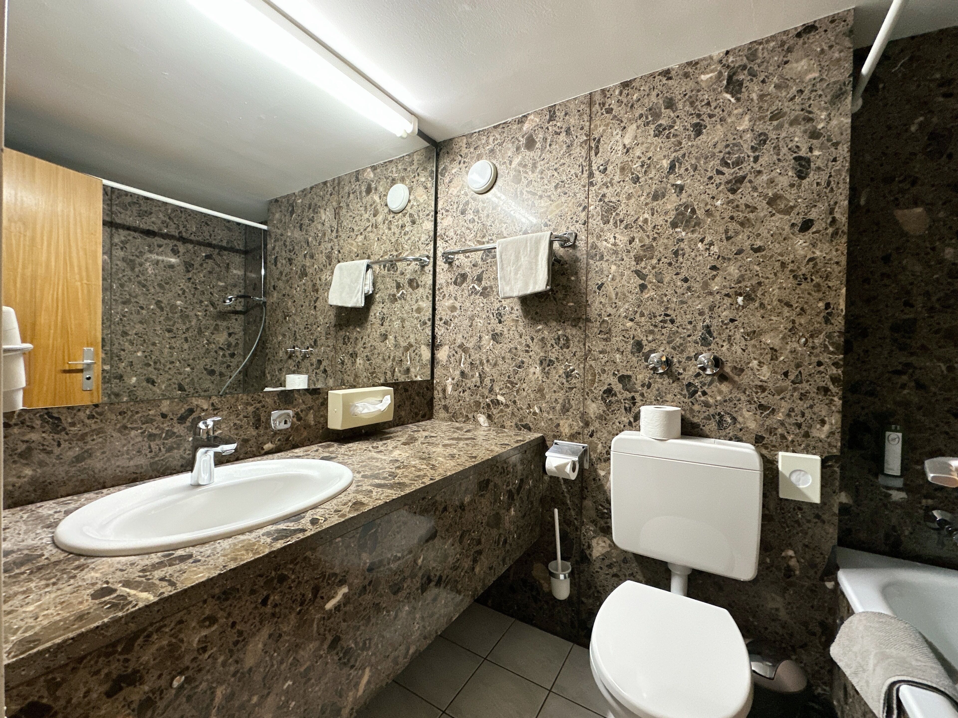 Ein Badezimmer mit Granit-Arbeitsplatten, einem weißen Waschbecken, einer Toilette und einem Spiegel.