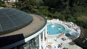 A rooftop pool area with a circular design, surrounded by lounge chairs and umbrellas, and a building with large windows in the background.