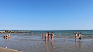 A beach with people in swimwear, a rocky breakwater, and calm waters.