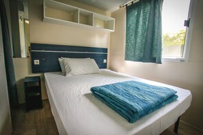 A neatly made bed with a folded blanket, a bedside table, and a headboard with built-in shelves. - Camping Parco Capraro (Jesolo)