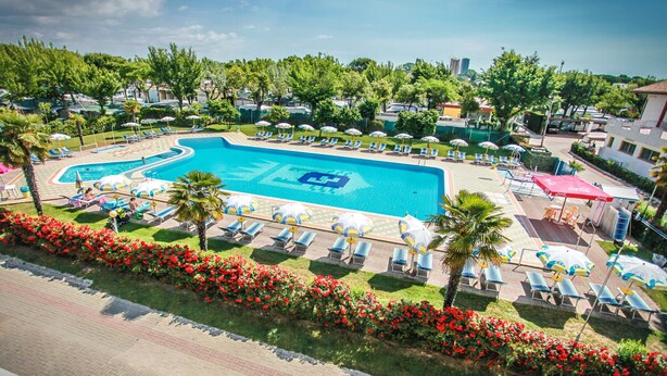 A swimming pool with lounge chairs and umbrellas, surrounded by greenery and a flower bed.