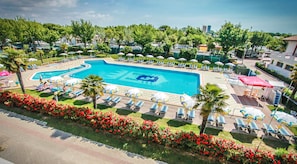 Ein Swimmingpool mit Liegestühlen und Sonnenschirmen, umgeben von Grünflächen und einem Blumenbeet.