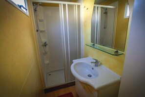 A bathroom with a glass shower enclosure, a white sink, and a mirror with a glass shelf. - Camping Parco Capraro (Jesolo)