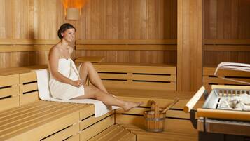 Una sauna con bancos de madera y una mesa con un cubo y cuchara de madera.
