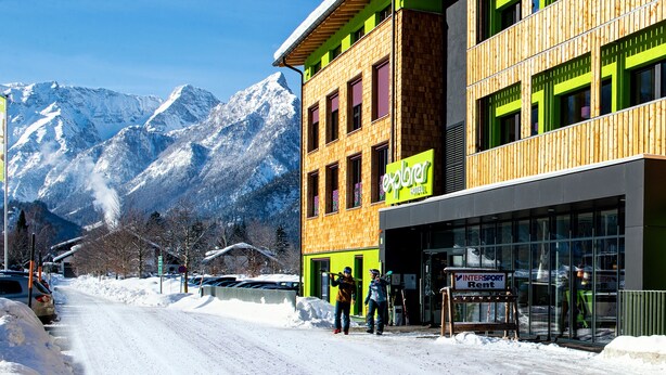 A hotel with a modern design, featuring a prominent green sign and a wooden facade.