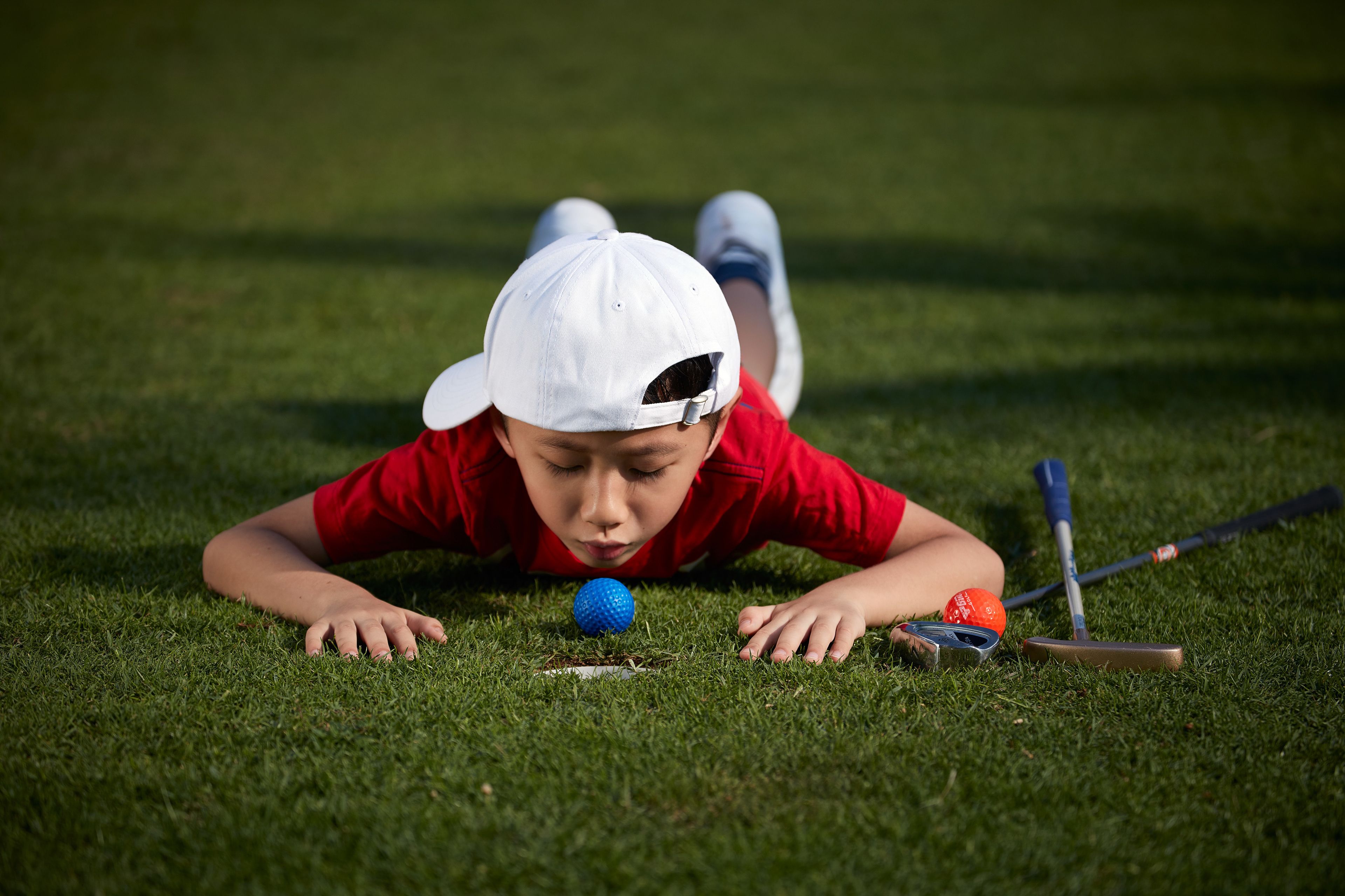 A person lying on grass with golf equipment.