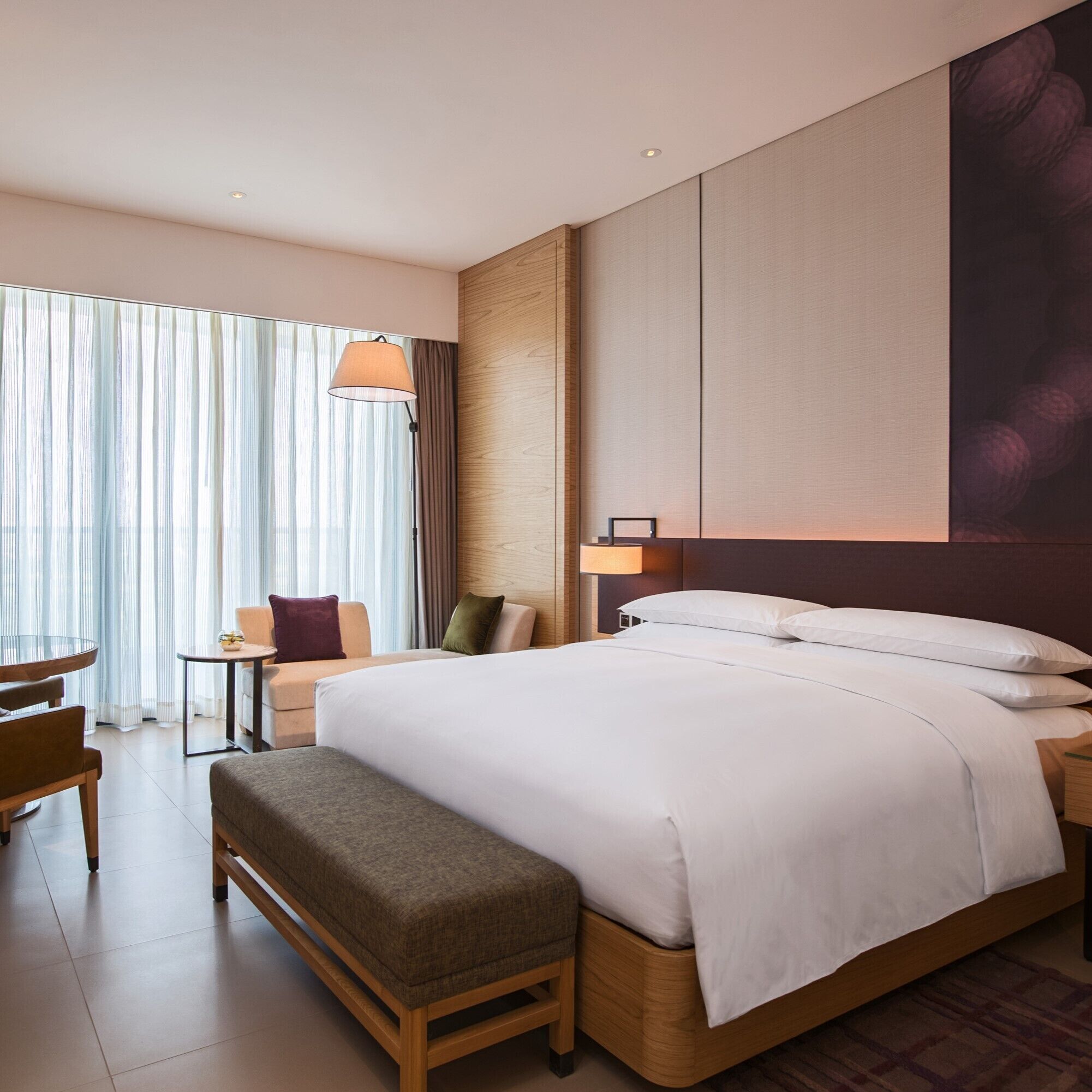 Ein Hotelzimmer mit einem großen Bett, einem Nachttisch, einer Lampe, einem Sessel, einem kleinen Tisch und einer Bank.